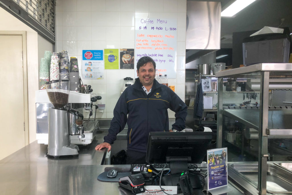Beaconhills College’s Food Service Operations Manager, Chetan Gaisas, stands smiling next to a coffee machine behind the counter of the school canteen.