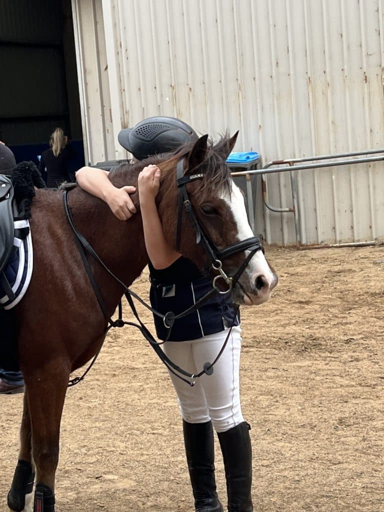 A student rider standing next to a horse and hugging it around the neck.