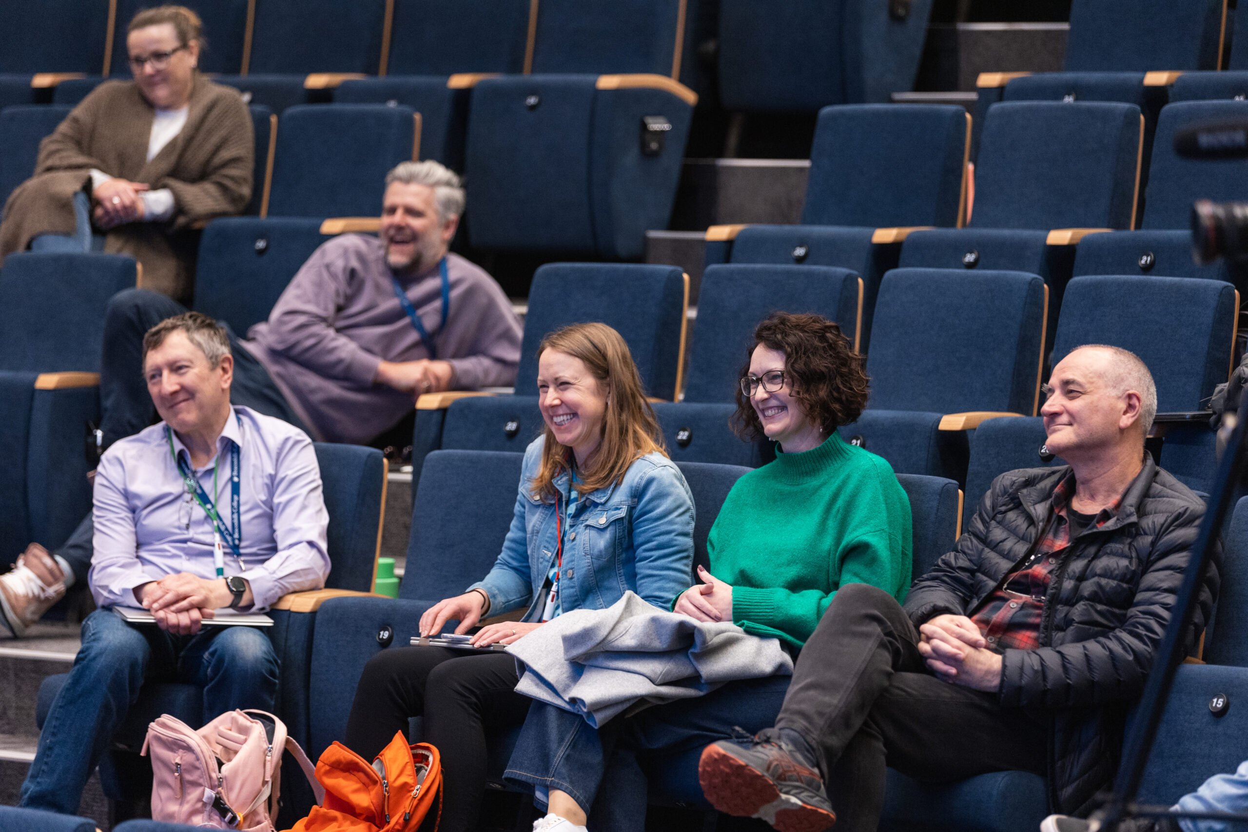 Six staff members sitting in theatre seating laughing